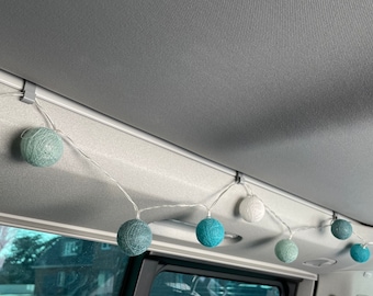 May include: String lights with spherical, textured shades in shades of teal, white, and gray are strung across the interior of a vehicle. The lights are attached to the ceiling with small, black clips, creating a decorative ambiance.