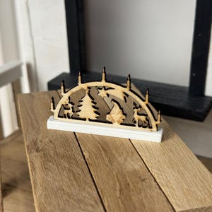 Könnte beinhalten: Weihnachtsdekoration aus Holz mit einem ausgeschnittenen Design eines Weihnachtsbaums, Sterns, Rentiers und Kerzen. Die Dekoration steht auf einem weißen Sockel und auf einer Holzoberfläche. Der Hintergrund umfasst einen schwarzen Rahmen.