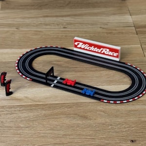 Könnte beinhalten: Ein Slotcar-Rennset mit einer ovalen schwarzen Bahn mit rot-weißen Rändern, zwei kleinen Rennwagen in Rot und Blau, einem schwarzen Zieltor, zwei schwarz-roten Handreglern und einem weißen Schild mit der Aufschrift Wichtel Race.