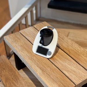 Könnte beinhalten: Ein weißer und grauer Mini-Küchenmixer mit einem schwarzen Deckel auf einem Holztisch.