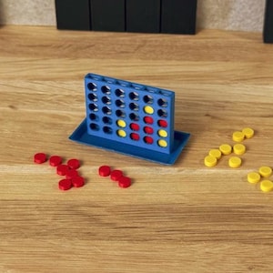 Könnte beinhalten: Ein blaues Kunststoff-Gitterspielbrett mit Basis, das eine vertikale Schlitzstruktur aufweist. Mehrere rote und gelbe kreisförmige Spielsteine sind in das Gitter eingesetzt, während weitere lose rote und gelbe Spielsteine um die Basis liegen.