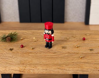 Peut inclure: Une petite figurine de casse-noisette portant un uniforme rouge vif avec des boutons blancs, une ceinture noire à boucle argentée, des bottes noires et un chapeau rouge assorti. La figurine a une moustache noire peinte.
