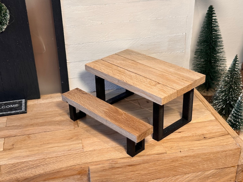 Peut inclure: Une table de pique-nique miniature en bois avec un cadre en m&eacute;tal noir. La table a une finition en bois naturel et mesure environ 38 cm de long.