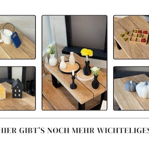 May include: A collection of miniature decorative items displayed on wooden surfaces. The items include vases with flowers, small houses, pumpkins, a bucket, and a candle holder. The text at the bottom reads "HIER GIBT'S NOCH MEHR WICHTELIGES".