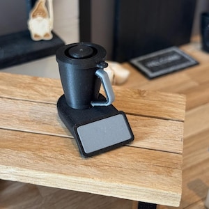Könnte beinhalten: Ein schwarzer und grauer Mini-Küchenmixer mit silbernem Sockel und Griff. Der Mixer steht auf einem Holztisch.