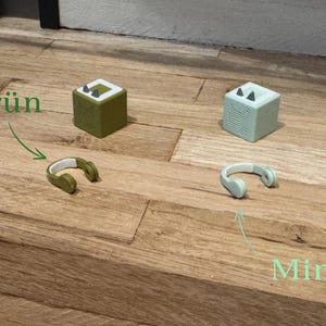 May include: Two small, cube-shaped speakers, one green and one mint green, with headphones next to each. The green speaker has the word "Gr&uuml;n" written above it, and the mint green speaker has the word "Mint" written below it.