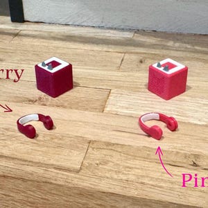 May include: Two red and white mini speakers with the words "Berry" and "Pink" written on the wooden surface below them.  A pair of red headphones are next to each speaker.