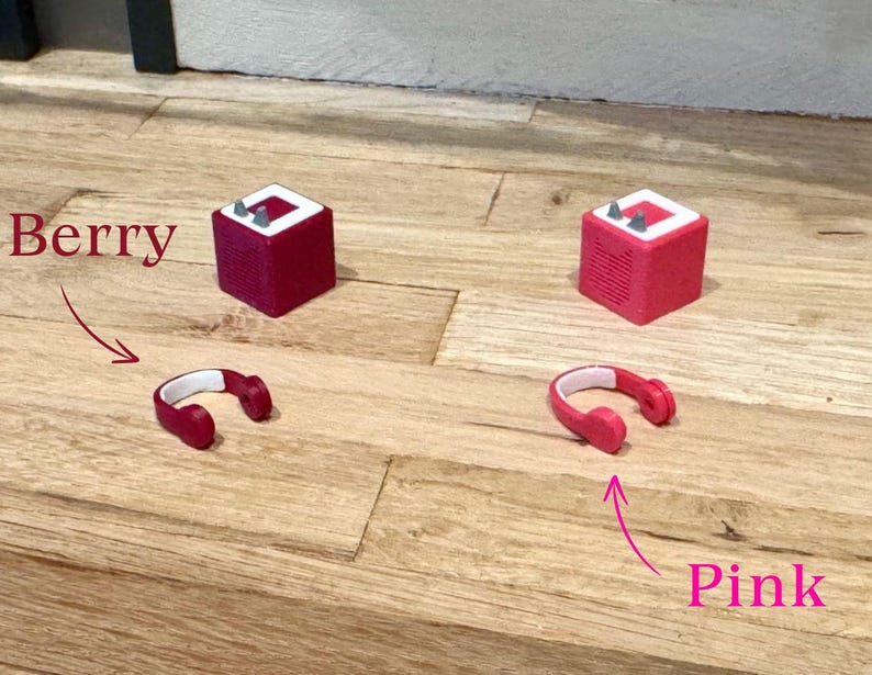 May include: Two red and white mini speakers with the words "Berry" and "Pink" written on the wooden surface below them.  A pair of red headphones are next to each speaker.