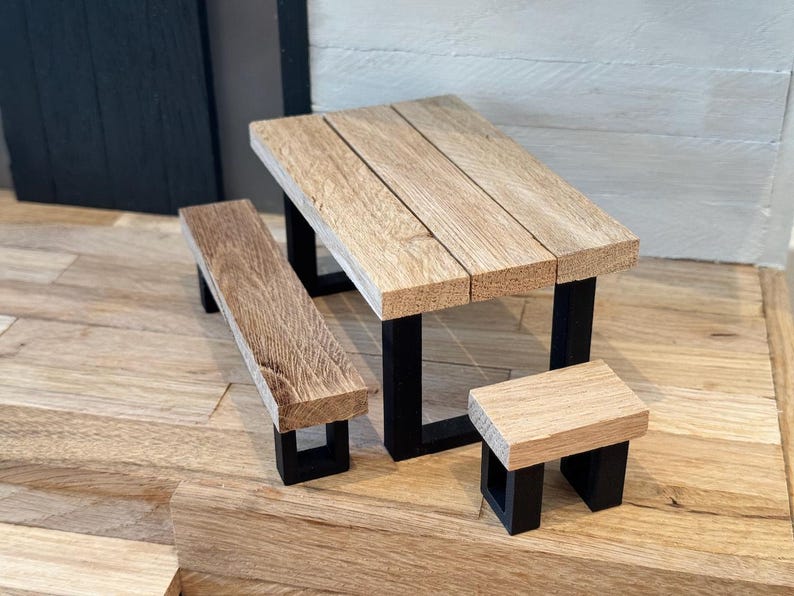 Peut inclure: Un ensemble de table de pique-nique en bois avec une table rectangulaire et deux bancs. La table et les bancs ont une finition en bois naturel et des pieds en m&eacute;tal noir.