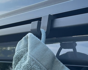 May include: A black plastic hook attached to a gray surface with a light blue towel hanging from it.