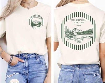 May include: A natural-colored t-shirt featuring a dark green graphic. The front displays a small circular design with a mountain and lake scene and the text "Lake Crew Your name". The back shows a larger version with "The Johnson Lake Trip".