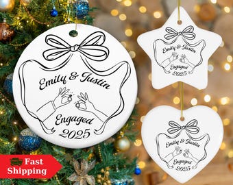 May include: White ceramic engagement ornaments in round, star, and heart shapes. Each ornament features a black line drawing of hands with rings, the names "Emily & Justin," and the year "2025." Gold string for hanging.
