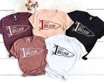 May include: Five short-sleeve crew neck t-shirts in maroon, peach, black, mauve, and white. Each shirt features a graphic of a pennant flag with the text "CAMP WILLIAM" and "YOUR TEXT HERE" printed in a contrasting color on the front chest area.