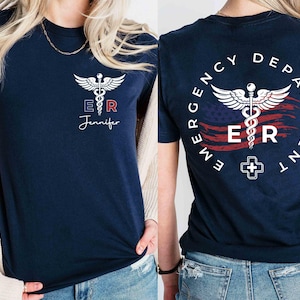 May include: A navy blue t-shirt with a white medical symbol and the letters "ER" on a red, white, and blue American flag design. The text "Emergency Department" is written in a circle around the flag. The shirt also has the text "ER Jennifer" on the front.