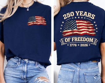 May include: Navy blue t-shirt with a distressed American flag graphic on the front and back. The back of the shirt features the text "250 YEARS OF FREEDOM" with the years "1776 2026" below the flag design.