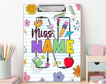 May include: A clipboard with a metal clip featuring a lined paper background, a large letter N, and the text Miss. NAME. The design includes colorful illustrations of a paint palette, pencil, book, apple, paper airplane, and various flowers.