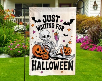May include: A white garden flag featuring a black skeleton illustration reclining against two orange jack-o'-lanterns while holding a purple drink. The text reads JUST WAITING FOR HALLOWEEN in black letters, accented by small black bats and colorful stars.