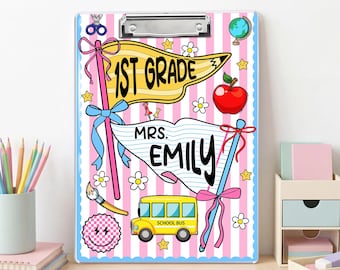 May include: A clipboard with a pink and white striped background featuring a yellow pennant flag labeled 1ST GRADE, a white flag labeled MRS. EMILY, a yellow school bus, a red apple, a globe, scissors, a paintbrush, and a smiley face icon.