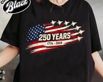 May include: Black t-shirt with a distressed American flag design. The flag graphic includes the text "250 YEARS 1776-2026" and stars. The shirt also has the words "COMFORT COLOR Black" in a circular design.
