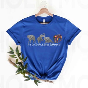 May include: A royal blue t-shirt with a graphic of four elephants. The elephants are all different colors and patterns. The text "It's Ok To Be A Little Different!" is printed below the elephants.
