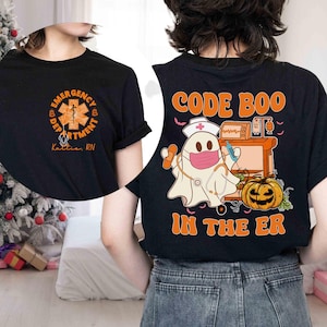 May include: Black t-shirt with a Halloween-themed design. The front features an orange and white emergency department logo and the text "Emergency Department". The back has a ghost nurse with the text "Code Boo In The ER".
