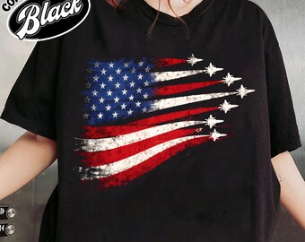 May include: Black t-shirt featuring a distressed American flag design with jets streaking across the red and white stripes. The top left corner has a Comfort Color Black logo.