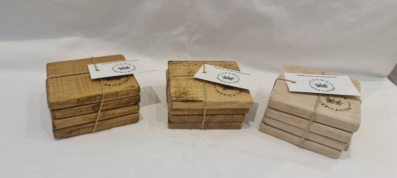 May include: Three stacks of square wooden coasters in varying shades of brown and tan. Each stack is tied with twine and has a small tag attached. The tags read "Thank you for purchasing from CROWN FABRICATION".