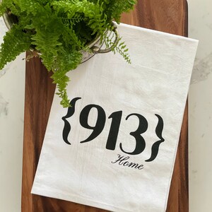 May include: White kitchen towel with black text that reads "{913} Home".
