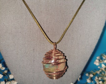 May include: A gold-toned wire cage pendant necklace with a multi-colored stone inside. The stone has swirls of brown, green, and white.