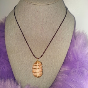 May include: A gold wire wrapped carnelian stone pendant on a brown leather cord necklace.