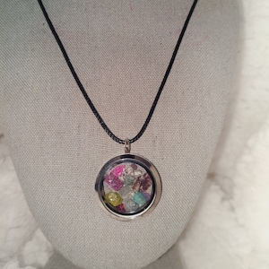 May include: A silver locket necklace with a black cord. The locket is filled with colorful, iridescent crystals.