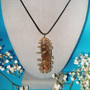 May include: A gold wire wrapped crystal pendant necklace with a brown cord. The crystal is clear with gold and red flecks.