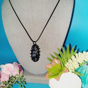 May include: Black and white stone pendant necklace on a black cord. The pendant is a long oval shape with a swirling pattern.