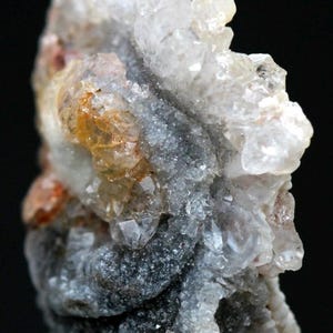 Puede incluir: Primer plano de un esp&eacute;cimen mineral con una estructura cristalina. La formaci&oacute;n rocosa presenta una mezcla de tonos claros, grises y anaranjados. La superficie tiene un aspecto rugoso y texturizado, con formaciones cristalinas visibles. El fondo es negro.