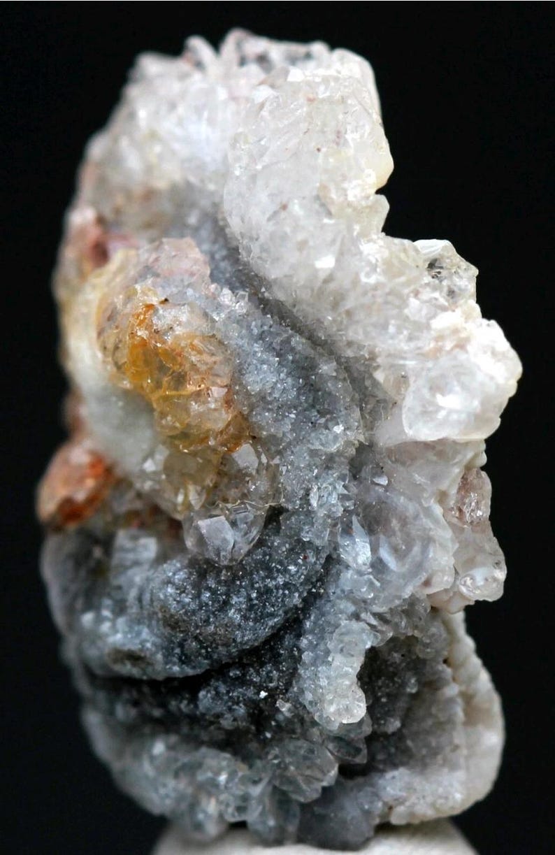 Puede incluir: Primer plano de un esp&eacute;cimen mineral con una estructura cristalina. La formaci&oacute;n rocosa presenta una mezcla de tonos claros, grises y anaranjados. La superficie tiene un aspecto rugoso y texturizado, con formaciones cristalinas visibles. El fondo es negro.