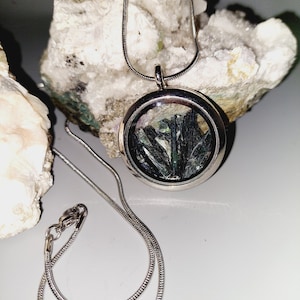 May include: A silver chain necklace with a round pendant containing a cluster of green and black crystals.