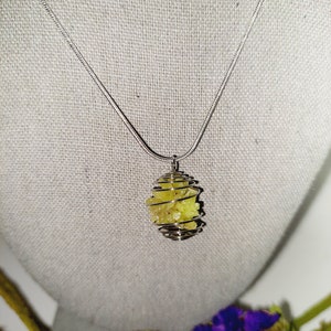 May include: A silver chain necklace with a yellow crystal caged in a silver wire pendant.