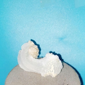 May include: A white, crystalline, mineral specimen with a unique, curved shape. The mineral has a smooth, polished surface and appears to be translucent.