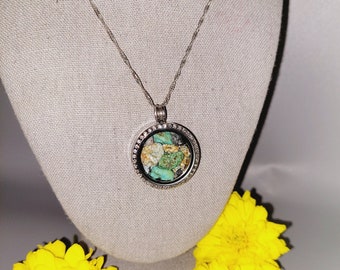 May include: A silver chain necklace with a round locket pendant. The locket is filled with small, colorful stones and has a silver border with small clear stones.