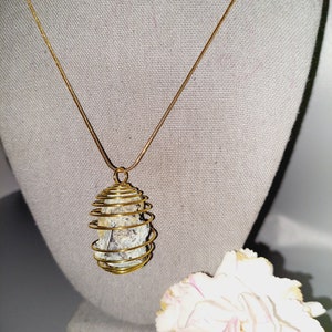 May include: A gold chain necklace with a pendant featuring a grey crystal encased in a gold wire cage.