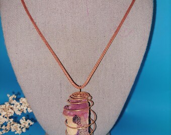 May include: A copper wire wrapped pendant necklace with a pink and white stone. The necklace is on a brown cord.