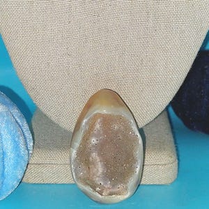 May include: A light brown agate geode with a crystal lined interior. The geode is smooth and polished, with a natural, organic shape.