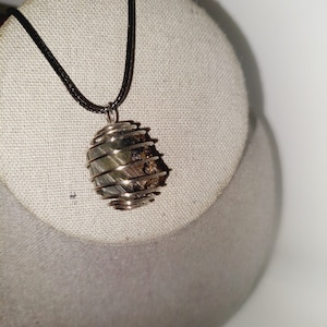May include: A silver wire wrapped pendant with a brown and green stone inside. The pendant is hanging from a black cord.