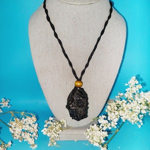 May include: A black stone pendant necklace with a brown wooden bead on a black cord. The necklace is displayed on a white mannequin.