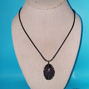 May include: A black gemstone pendant necklace with a black cord. The gemstone is wrapped in black wire.