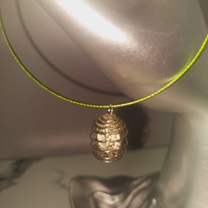 May include: A silver wire cage pendant with a clear crystal inside, hanging from a green string.