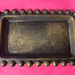 May include: A black tray with a gold metallic finish and a decorative beaded border. The tray is rectangular and has a slightly raised edge.