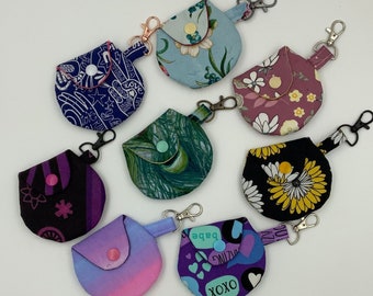 May include: Nine different fabric pouches with various patterns and colors. Each pouch has a small flap with a button closure and a metal ring for attaching a keychain. The pouches are made of cotton fabric and have a variety of designs, including floral, geometric, and abstract patterns.