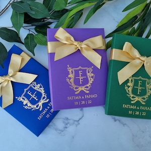 Op de afbeelding: Drie cadeaudozen met gouden strikken en gouden letters. De dozen zijn blauw, paars en groen. De letters op de dozen luiden "Fatima & Fahad 10 | 28 | 22".