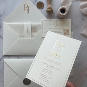 May include: A cream-colored wedding invitation suite featuring gold foil lettering, including a main invitation card, an RSVP card, and envelopes. The invitation displays the names Paige and James, event details for November 7th, 2026, and a wax seal stamp.